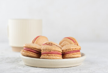 Vegan homemade caramel macarons with raspberry cream on shea butter with cup of tea. Sugar, lactose and gluten free.
