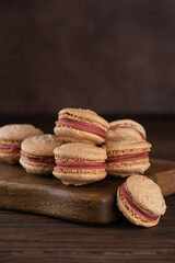 Vegan homemade caramel macarons with raspberry cream on shea butter on a brown wooden board. Sugar, lactose and gluten free. Vertical orientation.