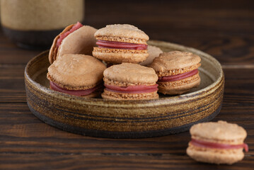 Vegan homemade caramel macarons with raspberry cream on shea butter in a plate on a brown wooden table. Sugar, lactose and gluten free.
