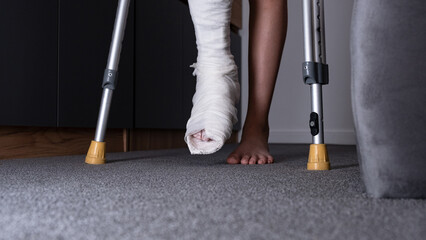 Teenager boy with injured broken leg in a plaster cast on the bed at home with crutches