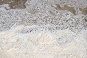 Detailed view of white sea foam forming delicate patterns as waves wash up on the sandy shore. This abstract nature-inspired image highlights the textures and fluidity of the ocean