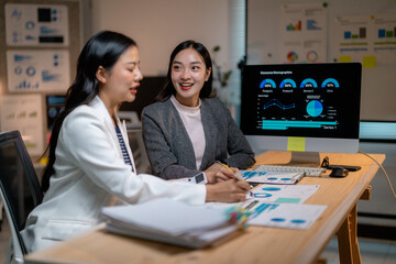 Asian businesswomen discussing marketing strategy analyzing charts on computer screen working late at night in office