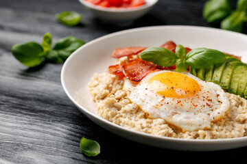 Savory Oatmeal breakfast with sunny side up fried egg, bacon and avocado. Healthy food