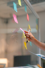 Businesswoman sticking colorful sticky notes on glass wall in office