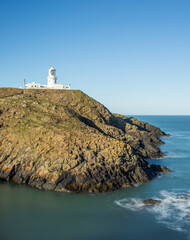 Strumble Head Lighthouse on the Pembrokeshire Coast in Wales with blue sky and calm sea