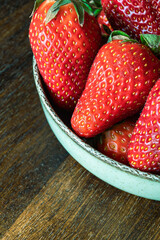 Fresh strawberries in bowl on dark wood background with copy space.