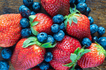Fresh strawberries and blueberries in macro detail on rustic background.