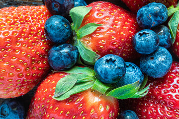 Strawberries surrounded by blueberries on wooden background, top view.