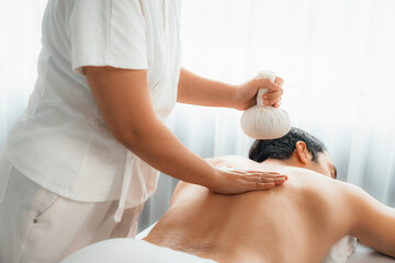 Hot herbal ball spa massage body treatment, masseur gently compresses herb bag on man body....