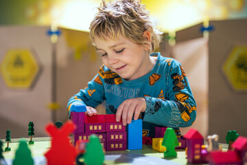 A young boy smiles as he plays in a playroom, building little houses with colorful building blocks, immersed in fun and creativity.