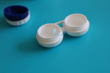 A contact lens lies on the case with solution on a light blue background. 