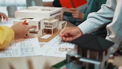 A vibrant architecture studio scene showing professionals engaged in model building and discussion. Various design sketches and physical models illustrate creative processes and teamwork. SACTR
