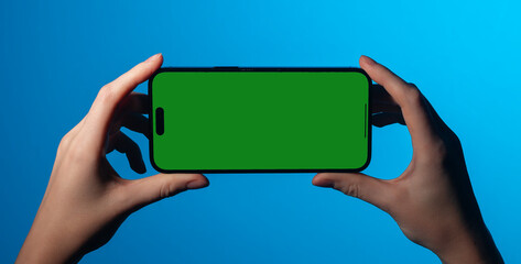 A woman holding smartphone in both hands, watching video or movie on screen. Modern device in horizontal view, displaying blank space for promotion or ad. Technology, app, and cellular gadget usage..
