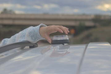 Hand placing a V16 emergency beacon on the roof of a broken-down vehicle. The emergency flasher is mandatory for replacing triangles in Europe. DGT Spain.