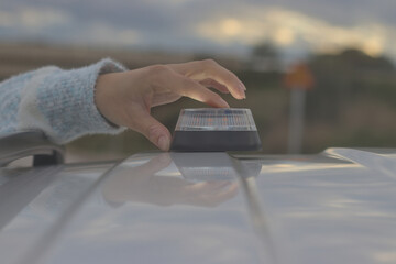 Hand placing a V16 emergency beacon on the roof of a broken-down vehicle. The emergency flasher is mandatory for replacing triangles in Europe. DGT Spain.