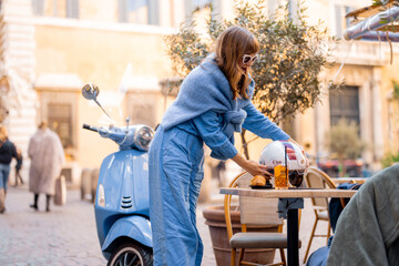 A fashionable Italian woman in a stylish blue outfit arrives on a scooter for an aperitivo at a...