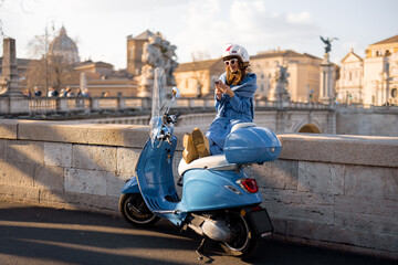 A fashionable woman enjoys a scenic view of Rome while relaxing on a blue scooter. With the citys historic architecture in the background, Italian lifestyle and adventure © rh2010