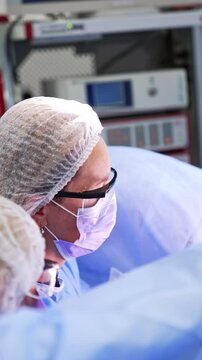 Female doctors wearing protective glasses work at the surgery. Professionals perform gynecologic operation in modern hospital. Vertical video.