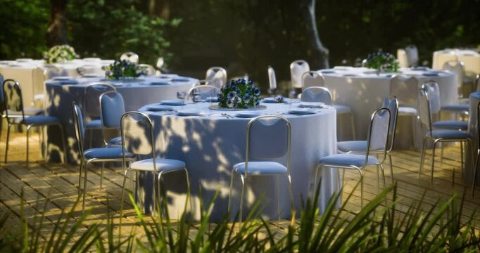 A serene outdoor dining setting features several round tables dressed in white tablecloths, adorned with fresh floral centerpieces. Soft light filters through the trees creating a tranquil atmosphere.