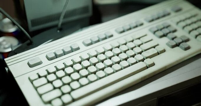 A vintage computer keyboard rests on a wooden desk, surrounded by old electronic devices, with soft light illuminating the scene, evoking a sense of nostalgia and technology history.