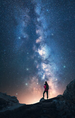 Glowing Milky Way and woman on mountain peak at starry night. Dolomites, Italy. Galaxy. Space landscape with silhouette of a girl, rocks, sky with bright stars. Milky Way and hiker. Vertical landscape