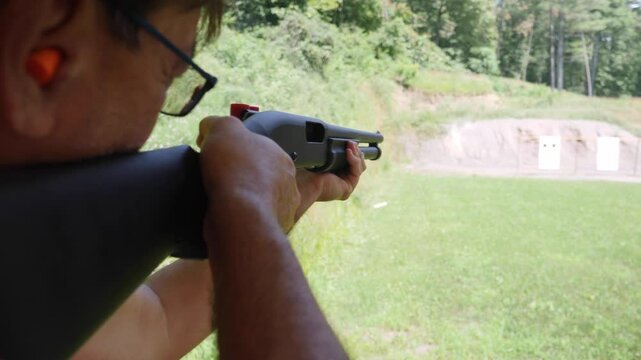 A man shoots a 12-gauge shotgun at an outdoor rifle range. With audio. Shot at 60fps for optional slow-motion.  	