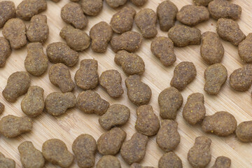 Close-up of cat food on a wooden surface, top view. A lot of small brown kibbles scattered around the scene
