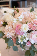 A wedding table centerpiece sits pretty in a gold compote bowl. The arrangement features white roses, ranunculus, and pastel carnations