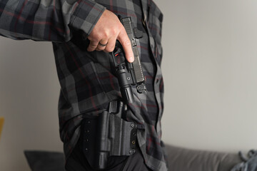 A man in a shirt pulls out a tactical pistol with a flashlight from a Kydex holster.