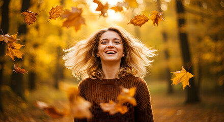 Smiling woman with blonde hair in a brown sweater surrounded by falling autumn leaves outdoors