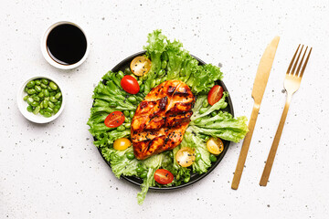 Healthy diet dinner concept. Fresh green salad with edamame beans and cherry tomatoes and chiken breast with teriyaki sauce on white stone background top view.