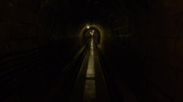 Walking through dark, wet corridor with reflective puddles on the floor, illuminated by faint, distant lights, highlighting the arched ceiling and narrowing perspective. 