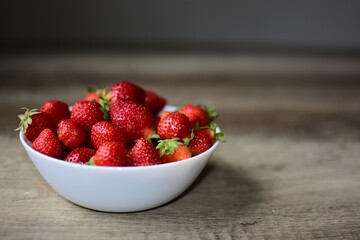Fresh strawberries bowl on a wooden table front view. Full bowl of red berries in ambient light.