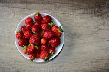 Fresh strawberries bowl on a wooden table top view. Full bowl of fresh red berries with copy space.