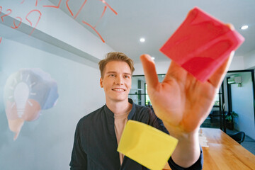 Professional caucasian businessman writing marketing idea by using mind map and sticky notes on glass board at modern meeting room. Creative business and planing concept. Closeup. Immaculate.