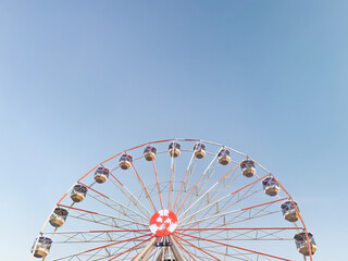 Fototapeta premium bright red and white Ferris wheel against clear blue sky. minimalistic composition with copy space. summer design, travel, amusement park