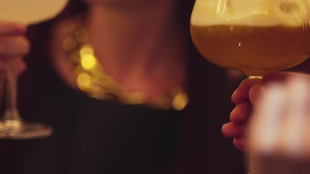 Closeup beautiful woman making a toast mixed passion fruit smoothie cocktail with friend holding glass in coconut smooth fizzy drink at nighttime warm light at nightclub counter bar party. Vinosity.