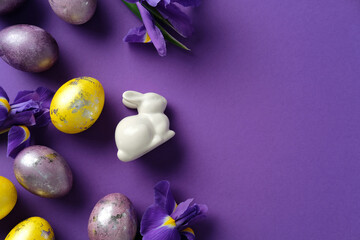 Easter flat lay composition with painted eggs, purple irises, and a ceramic bunny on a purple background