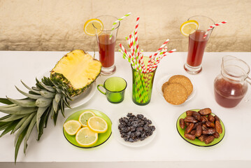 Healthy food on table fresh sliced ​​pineapple, lemon wedges, dates, cookies and colorful straws in glasses with juice at party at home