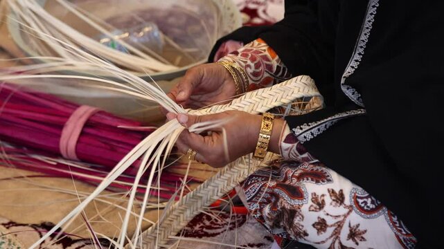 Emirati woman artisan weaving traditional al Khous using dried palm leaves, close up on hands. UAE heritage and sustainable craft concept.