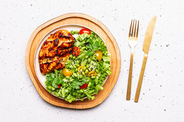 Healthy diet dinner concept. Fresh green salad with edamame beans and cherry tomatoes and chiken breast with teriyaki sauce on white stone background top view.
