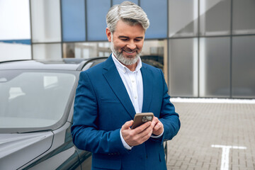 Businessman using his smartphone while standing at dealership