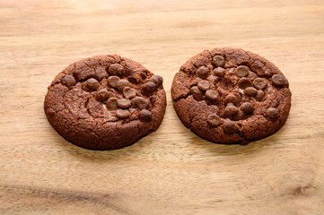 Two warm chocolate chip cookies sit side by side on a wooden surface, showcasing a rich brown color and gooey chocolate pieces. They are perfect for a sweet treat