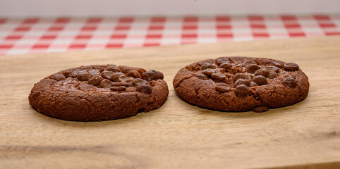 Two warm chocolate chip cookies sit side by side on a wooden surface, showcasing a rich brown color and gooey chocolate pieces. They are perfect for a sweet treat