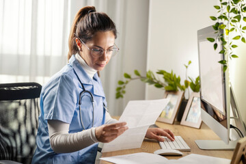 Young professional female doctor sitting at home office with test results and paperwork and...