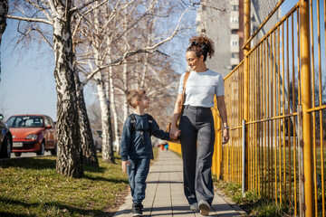Full length of a mother walking with her schoolboy on a city street.