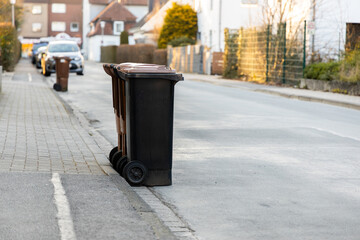 A full trash bin for bio waste stands on the sidewalk next to the street. day of removal of bio...