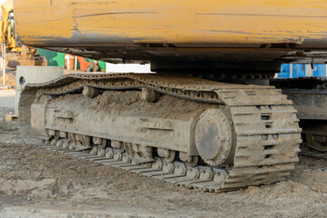 Close up of dirty track pad and rollers on a yellow excavator in sunlight