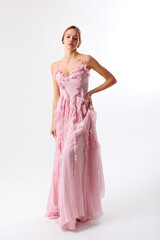 Elegant model poses in a flowing pink dress against a simple backdrop during a fashion shoot