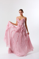 Fototapeta premium Elegant model showcasing a flowing pink gown in a minimalist studio setting during a fashion shoot